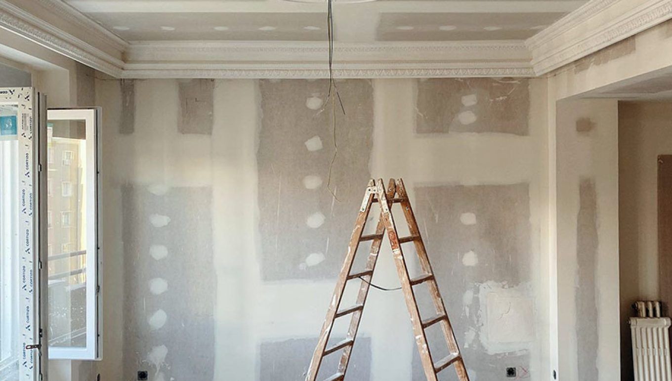 Habitación en proceso de reforma integral, con una escalera y paredes de pladur al fondo. Arriba, se puede observar un techo con molduras de escayola.
